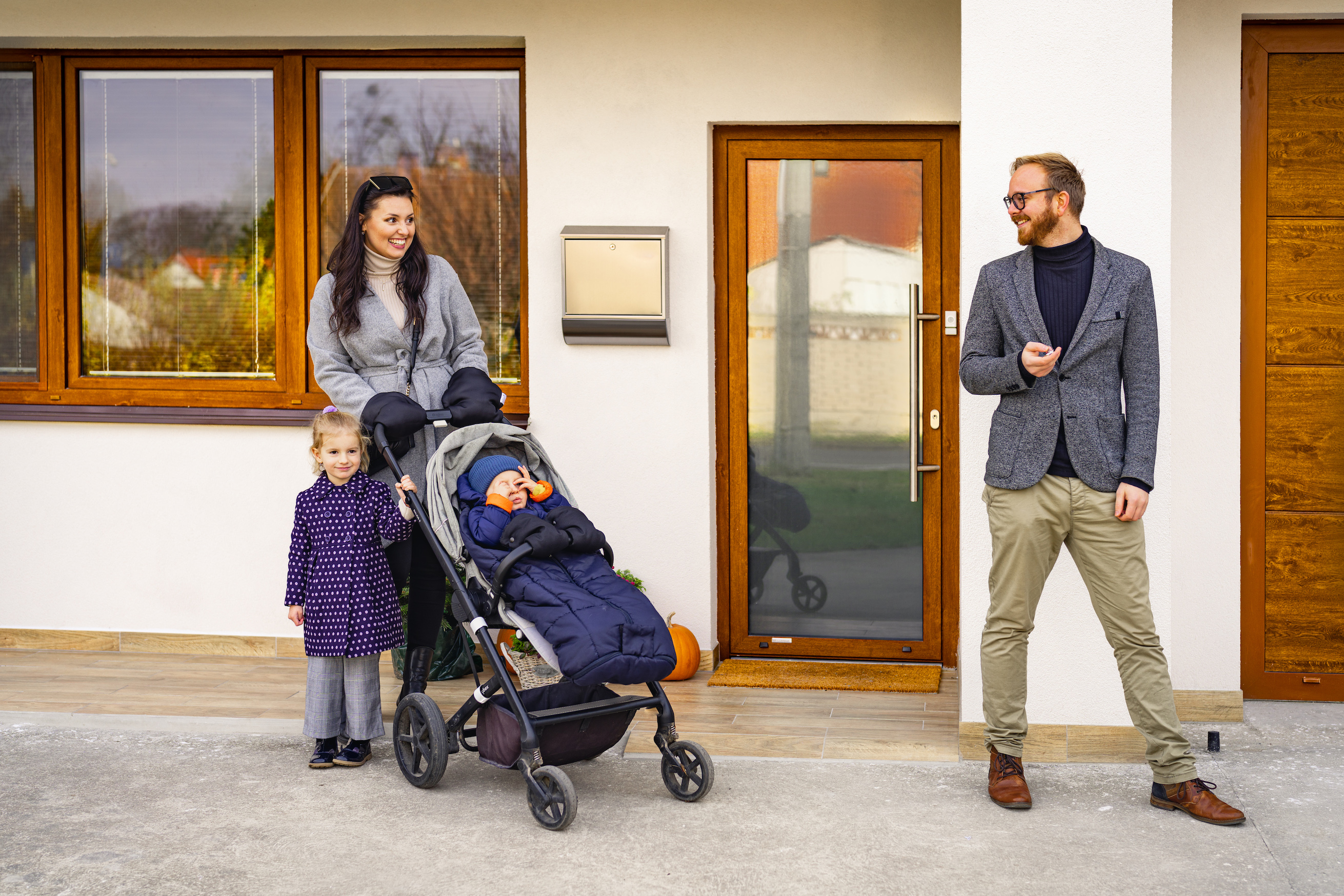 Mladá rodina před vchodovými dveřmi do rodinného domu