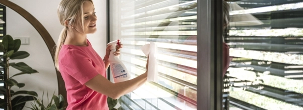 Žena umývá velká francouzská okna papírovou utěrkou a sprejem