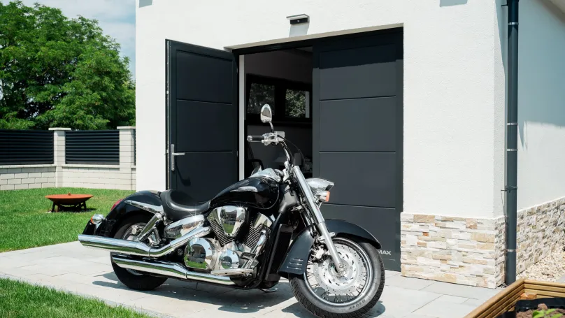 Černá garážová vrata u moderního domu s motocyklem před nimi